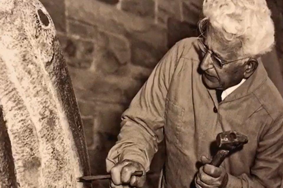 Black and white image of Henry Dispirito at work on a sculpture, with hammer and chisel in hand.